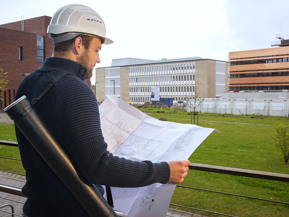 Ein Mann mit Schutzhelm, der auf einen ausgefalteten Gebäudeplan schaut